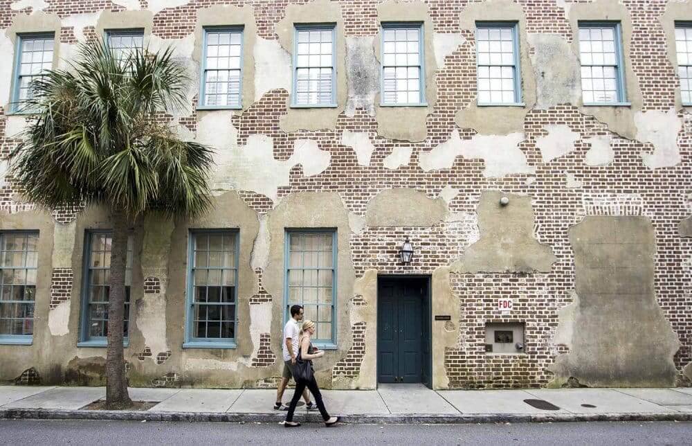 couple walking on a street in front of a brick building near goddard point hope apartments charleston south carolina dylan-mullins-hbpwn9dylgg-unsplash