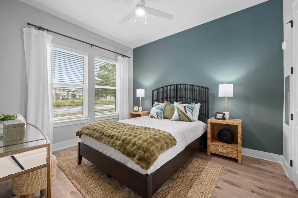 Model bedroom at our apartments for rent in Charleston, SC, featuring wood grain flooring and large windows.